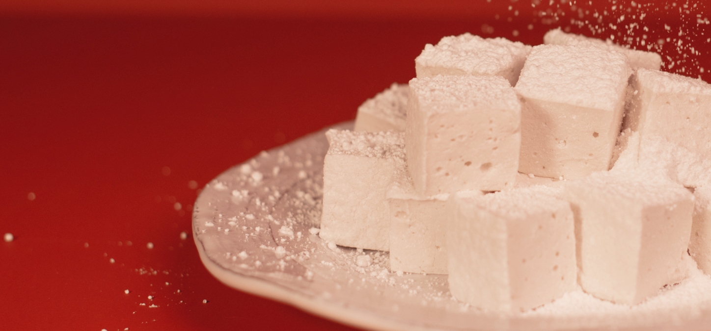 homemade marshmallows stacked on a plate sprinkled with powdered sugar