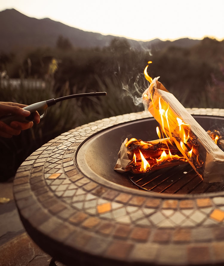 Duraflame OUTDOOR firelogs burning in an outdoor fire pit with hand holding a duraflame flex-neck utility lighter