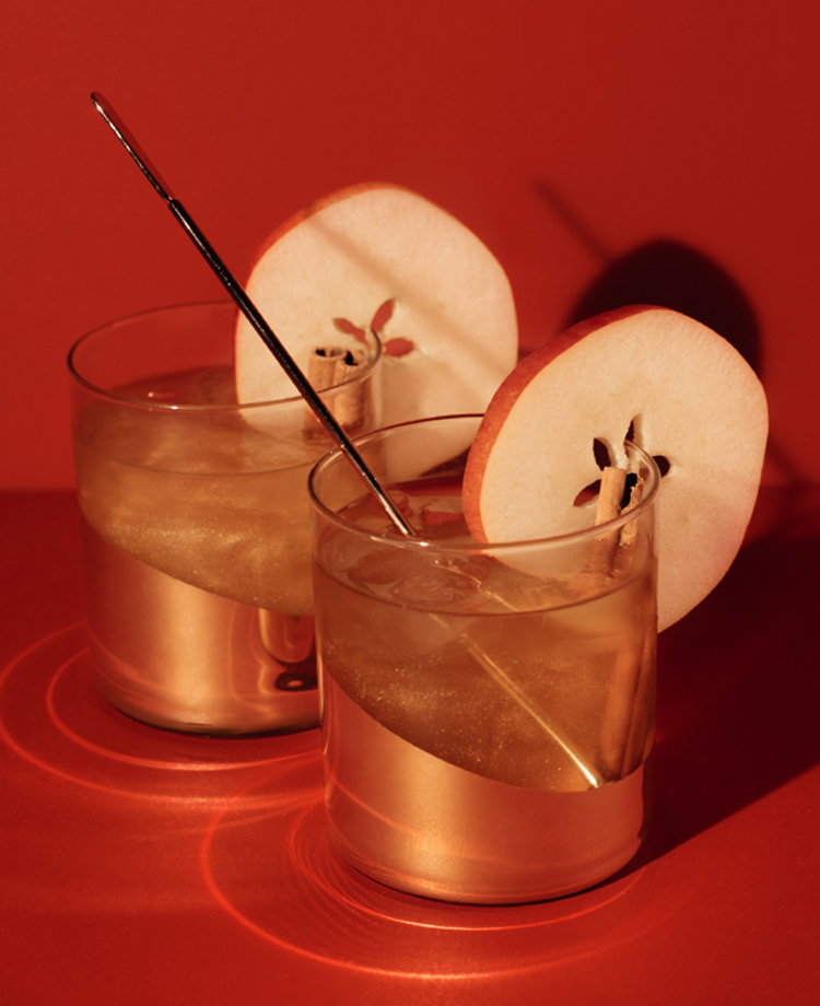 Two cocktails with apple garnishes with a red background