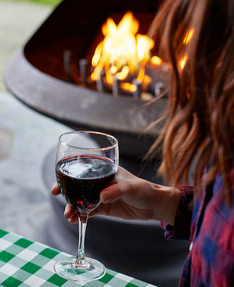 Woman holding glass of wine, enjoying a duraflame Crackleflame fire in a backyard fire pit