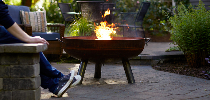 Backyard scene with person stretching legs next to large firepit burning duraflame OUTDOOR firelogs