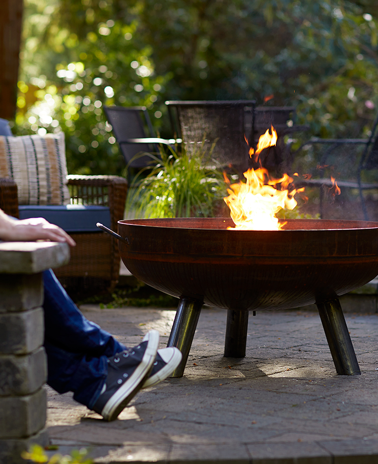Backyard scene with person stretching legs next to large firepit burning duraflame OUTDOOR firelogs