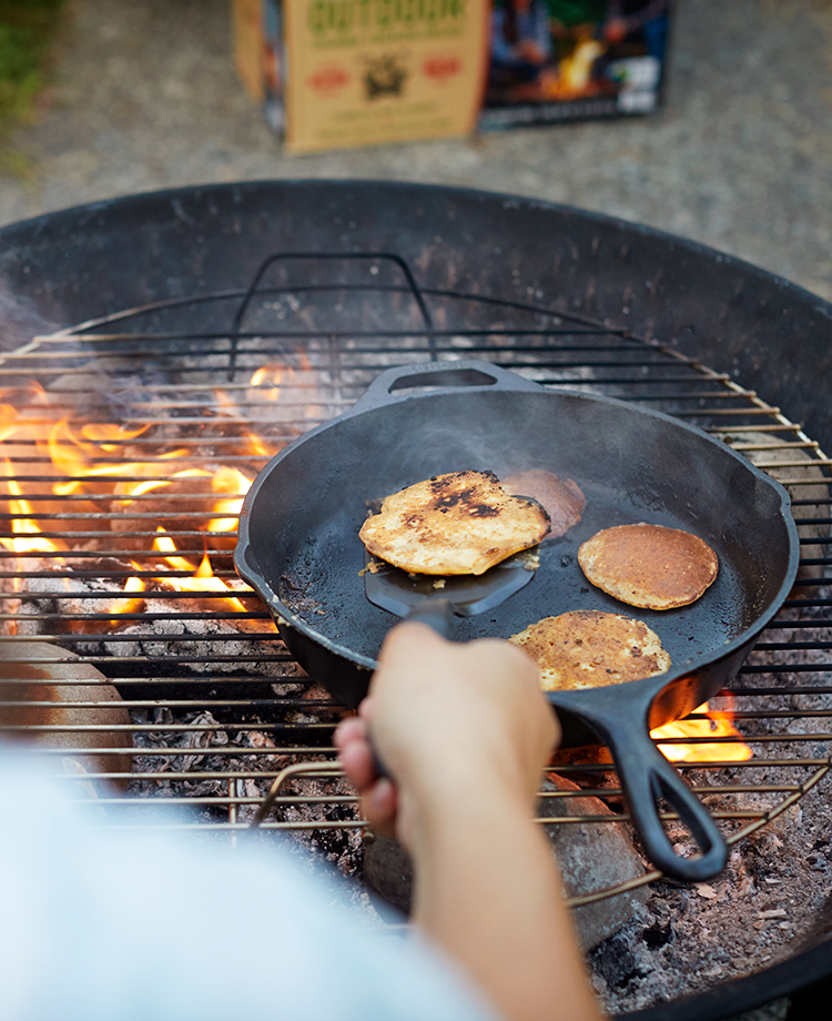 Person flipping pancakes in a griddle over campfire of burning duraflame OUTDOOR firelogs 