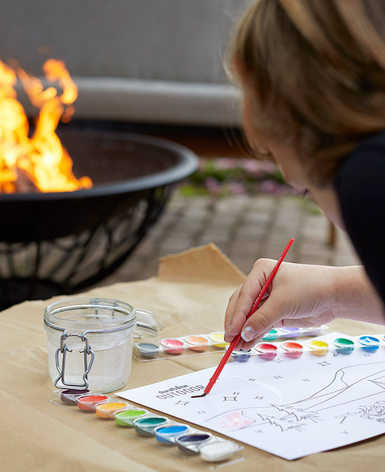 Person painting in the backyard with a duraflame fire in a fire pit in the background