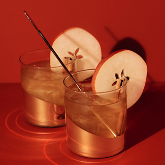 Two cocktails with apple garnishes with a red background