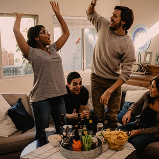 Group of friends with drinks and snacks high-fiving each other in the living room watching the big game