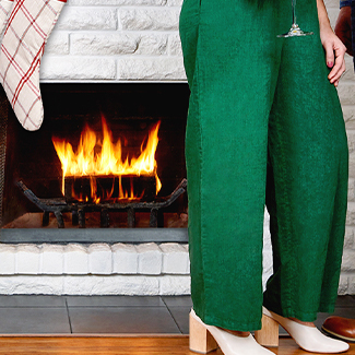 woman in holiday green slacks standing next to duraflame fire with stocking on hearth