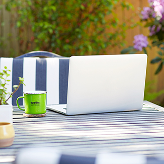 Backyard scene with laptop on patio table next to a green Duraflame brand mug