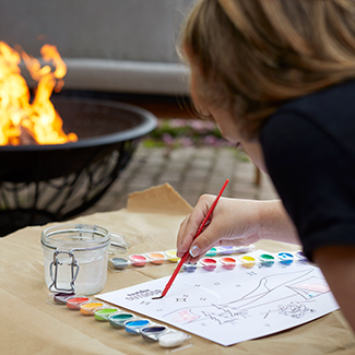 Person painting in the backyard with a duraflame fire in a fire pit in the background