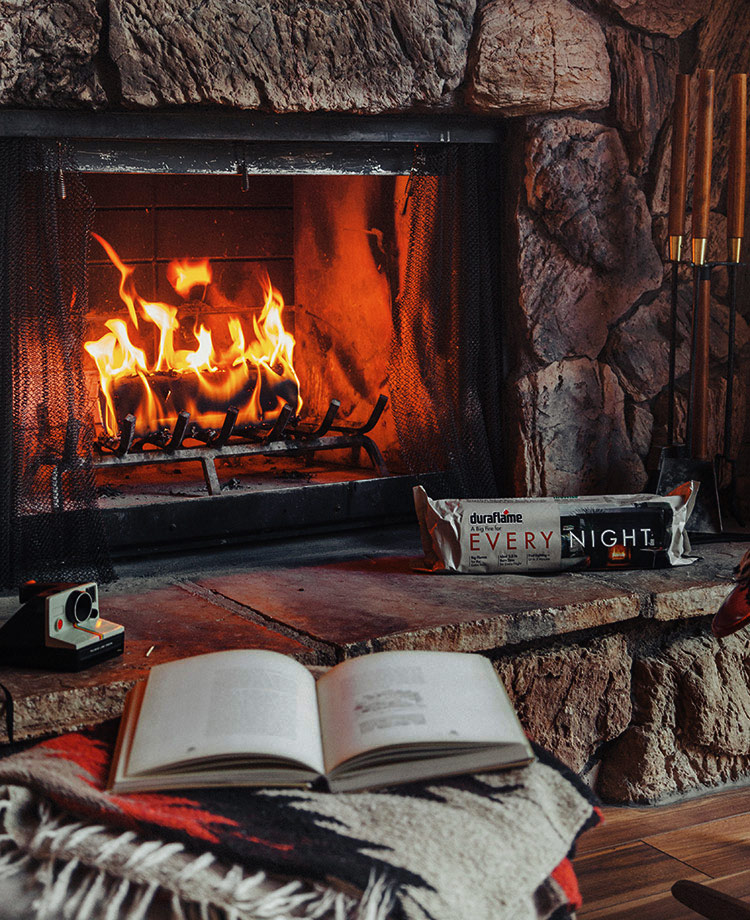 Blazing fire in fireplace with Every Night firelog on the side of fireplace and reading nook in forefront