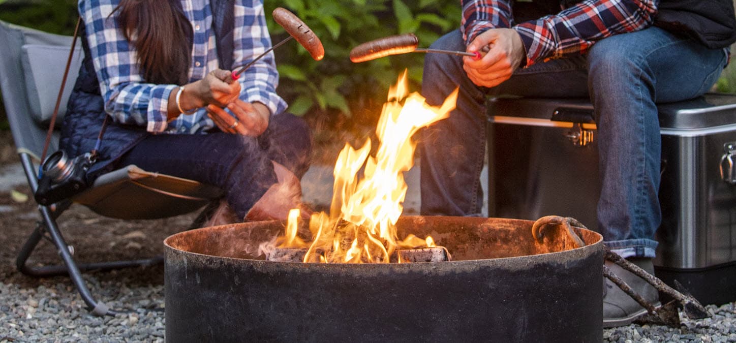 Couple roasting hot dogs over duraflame OUTDOOR firelogs in a camping fire pit