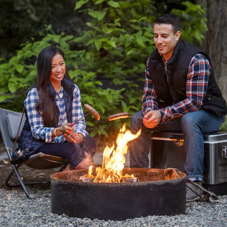 Couple roasting hot dogs over duraflame OUTDOOR firelogs in a camping fire pit