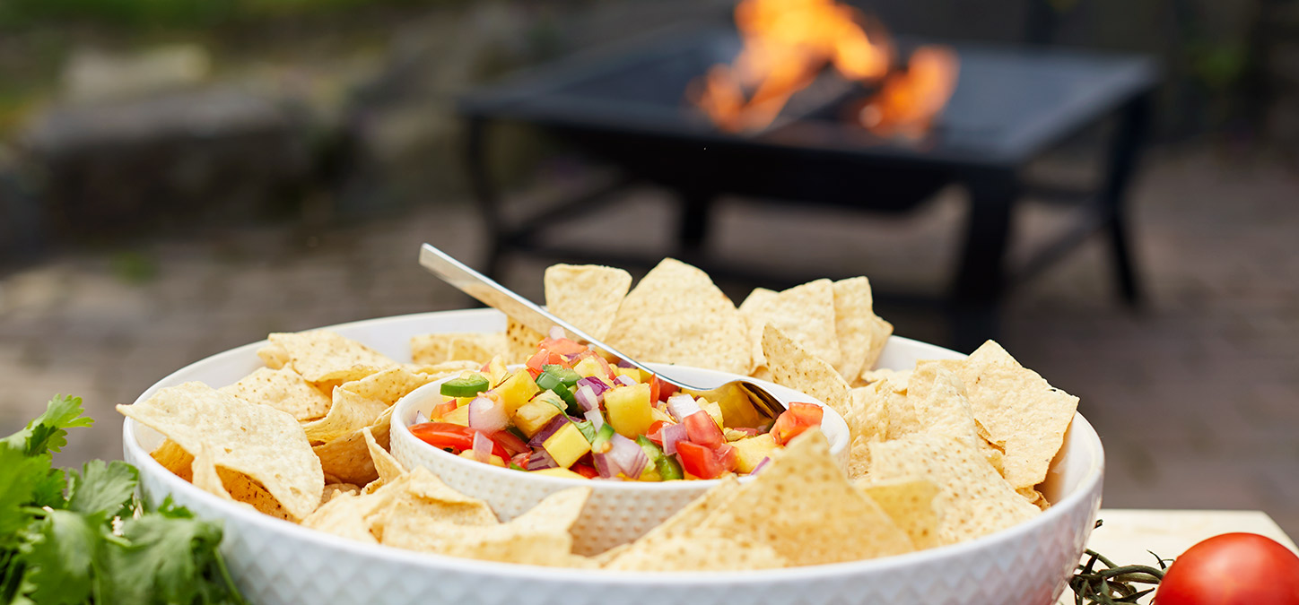 Grilled Pineapple Salsa and chips in a bowl with a Duraflame fire in fire pit in the background