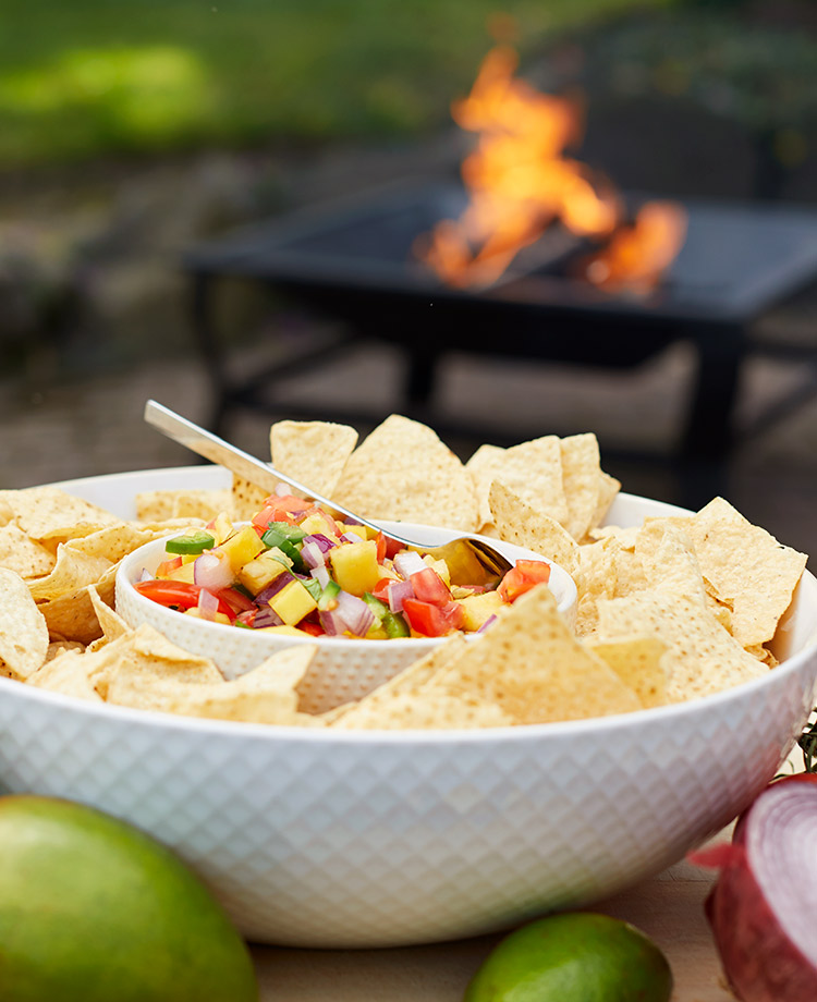 Grilled Pineapple Salsa and chips in a bowl with a Duraflame fire in fire pit in the background