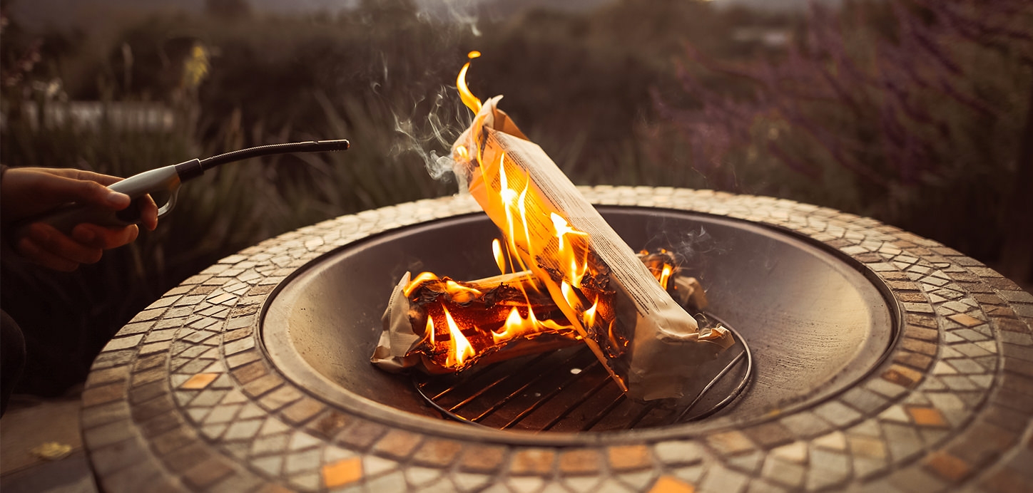 Duraflame OUTDOOR firelogs burning in an outdoor fire pit with hand holding a duraflame flex-neck utility lighter
