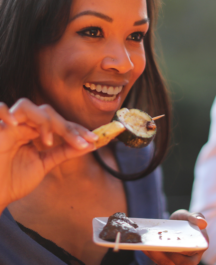 Woman smiling with a plate of appetizers and a vegetable skewer in her hand