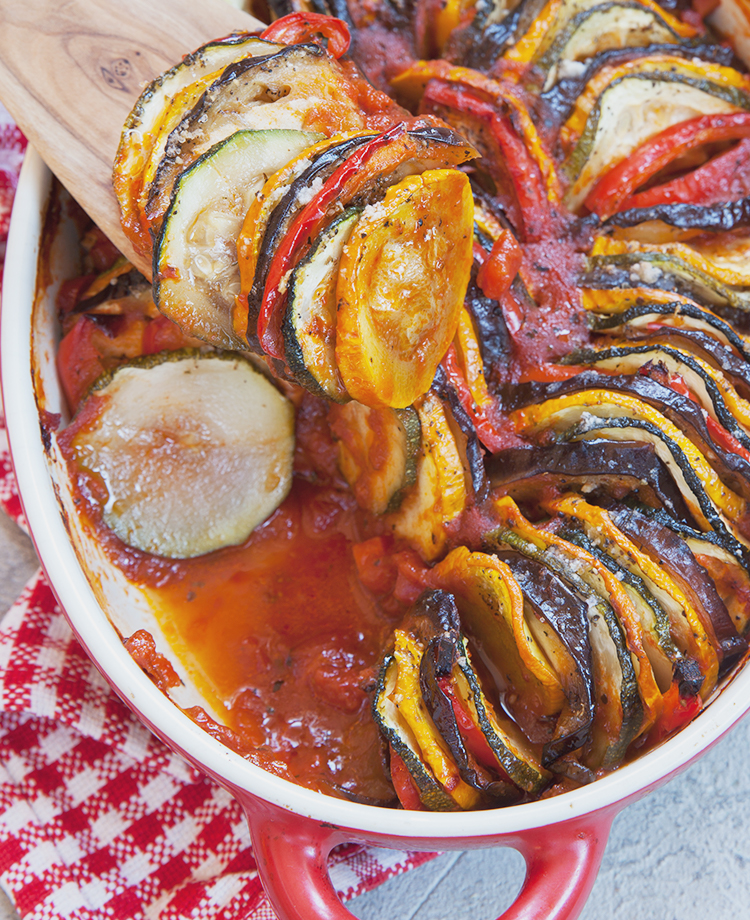 Ratatouille baked in a red casserole dish with closeup of sliced vegetables on wooden spoon