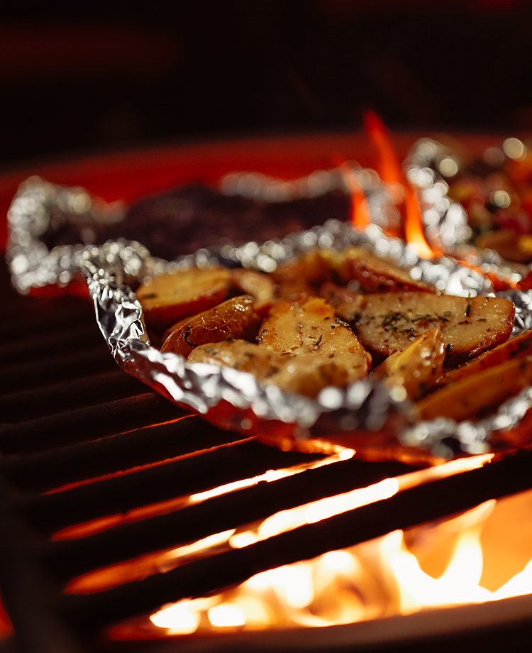 Roasted Potatoes and carrots on tin foil atop a grill and live fire