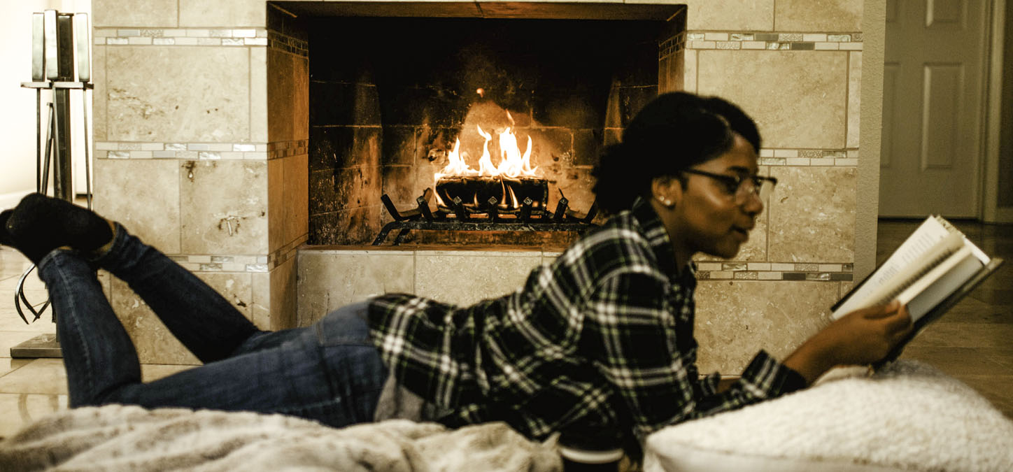 Woman lying on pillow reading a book in front of a duraflame fire