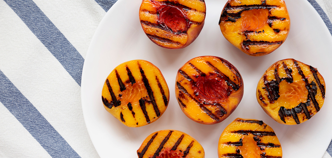 Pitted and halved peaches with grill marks on a white plate
