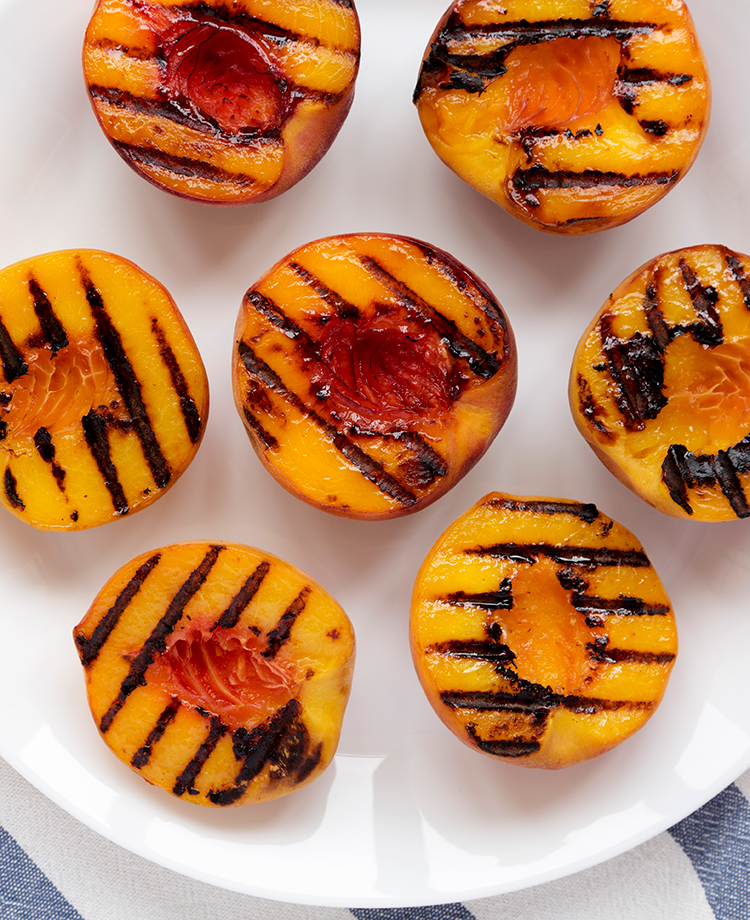 Pitted and halved peaches with grill marks on a white plate