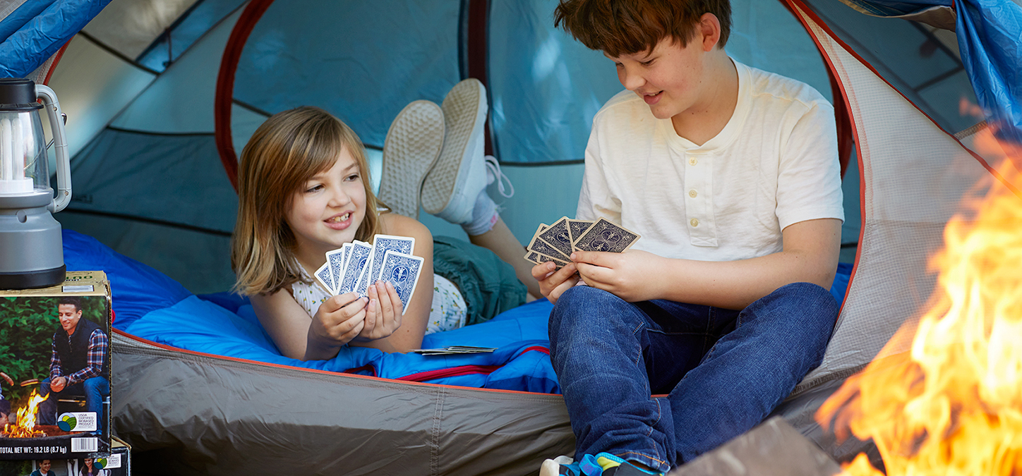 Kids backyard camping in tent, playing cards while enjoying duraflame OUTDOOR firelogs burning in fire pit