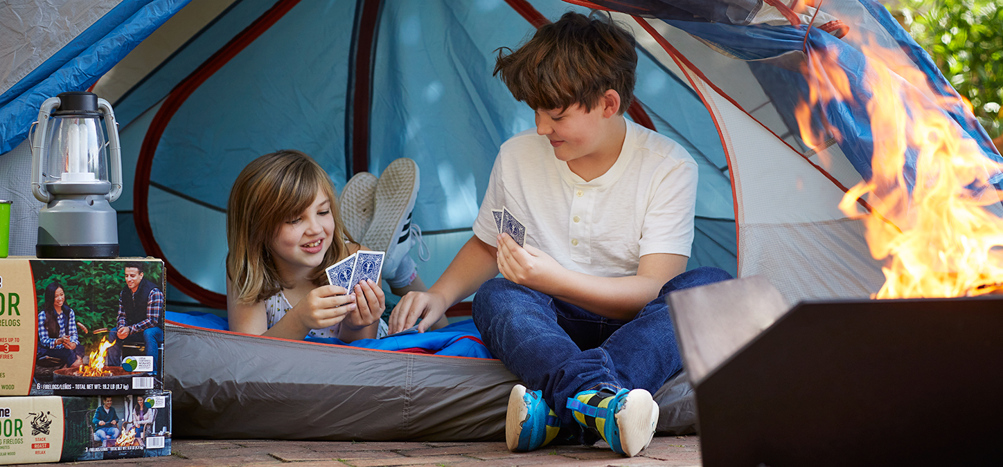 Kids backyard camping in tent, playing cards while enjoying duraflame OUTDOOR firelogs burning in fire pit