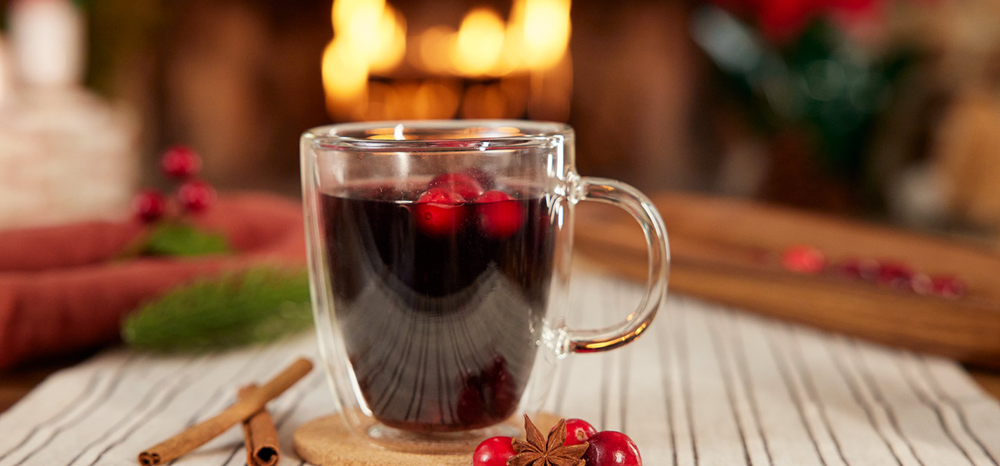 Libation in a glass mug with mulled wine and cranberries, with blazing fire in the fireplace in the background