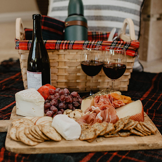 Charcuterie cheeseboard on blanket with wine and picnic Basket in background