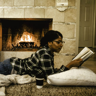 Woman lying on pillow reading a book in front of a duraflame fire