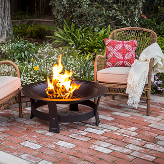 Backyard brick patio with two chairs, with pillows and a blanket next to a  fire pit burning duraflame OUTDOOR firelogs