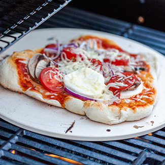 Pizza topped with mushrooms, tomatoes, onions & mozarella on a pizza stone on a grill 