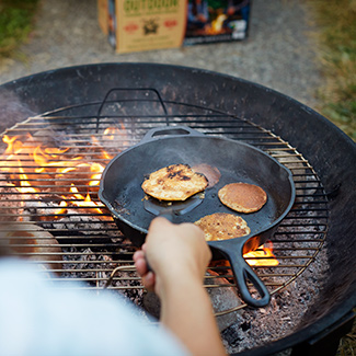 Person flipping pancakes in a griddle over campfire of burning duraflame OUTDOOR firelogs 