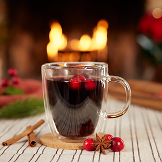 Libation in a glass mug with mulled wine and cranberries, with blazing fire in the fireplace in the background