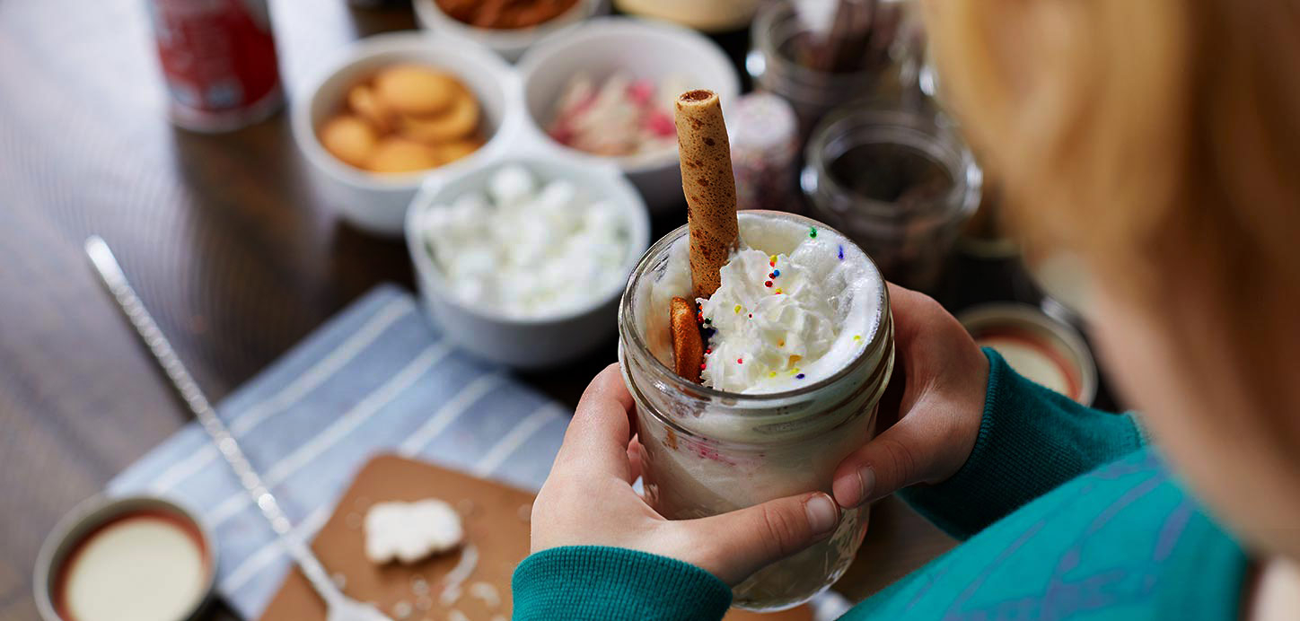 Hot cocoa bar with marshmallows, cookies and other toppings, and a kid holding his cup of hot cocoa