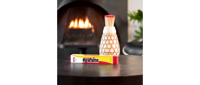 Box DURAFLAME® SAFETY MATCHES with decorative vase holding long stem matches and fire burning in hearth in background